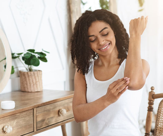 Woman sitting in a chair wearing a white top checking the sensitive skin on her elbow.