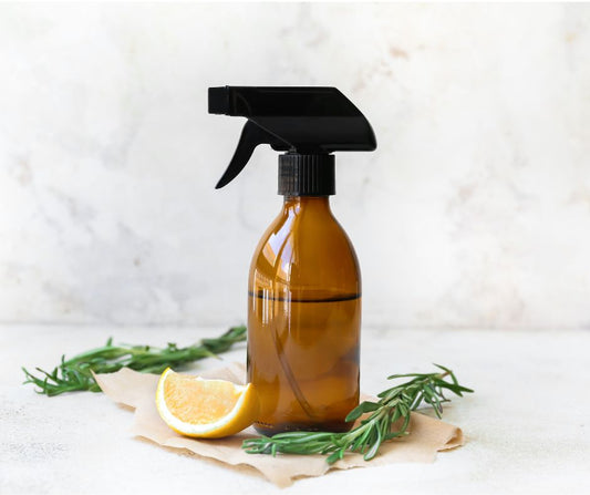 An amber spray bottle next to a lemon wedge and rosemary sprigs.