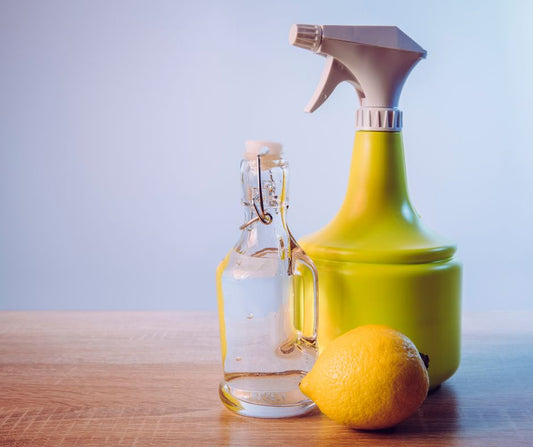 Yellow and white spray bottle, clear glass bottle and a lemon on a wood table.