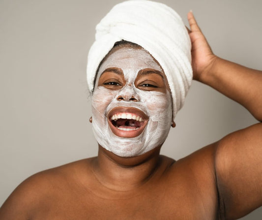 A laughing woman with her hair wrapped in a towel while wearing a face mask.