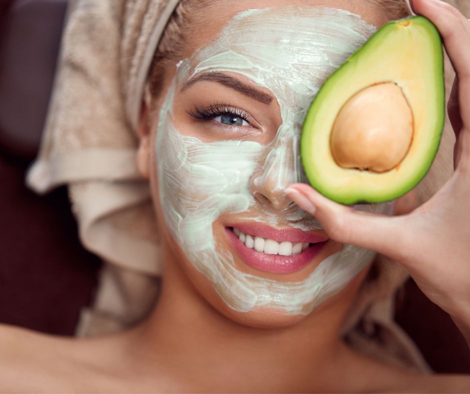 A woman wearing a face mask and a towel covering her hair hold half an avocado in front of her face.