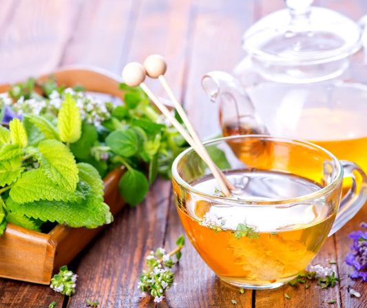 A clear glass tea set next to fresh herbs.