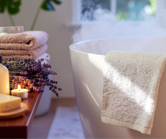Steam rising from a tub next to a table with a candle, lavender sprigs and towels on it.