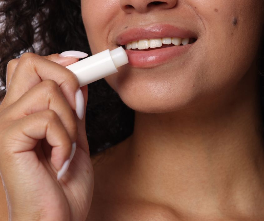 A smiling woman putting on lip balm.