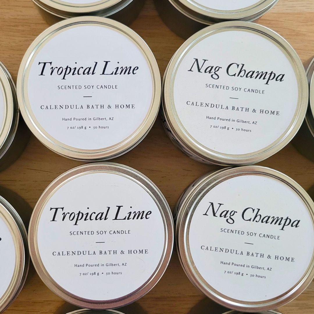 Candle tins labeled 'Tropical Lime' and 'Nag Champa' on a wooden surface.